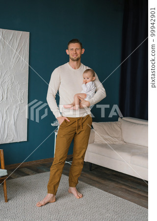 The young man is happy and holds his six-month-old son in his arms in his house The young man is happy and holds his six-month-old son in his arms in his house 99942901
