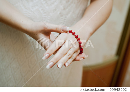 The bride puts on a red bracelet on her hand. close-up of hands The bride puts on a red bracelet on her hand. close-up of hands 99942902