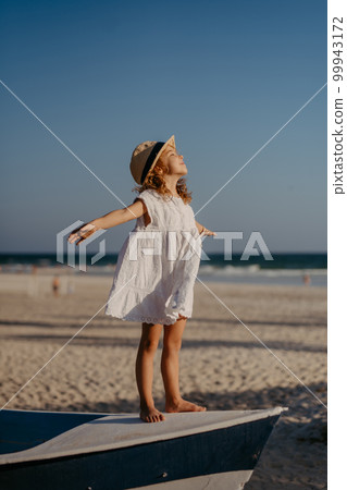 Little girl in summer dress and hat enjoying time at sea. Little girl in summer dress and hat enjoying time at sea. 99943172