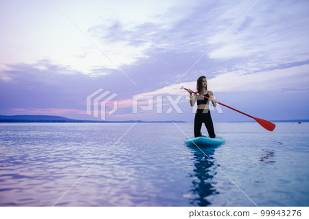 Young beautiful girl surfer paddling on surfboard on the lake at sunrise 99943276