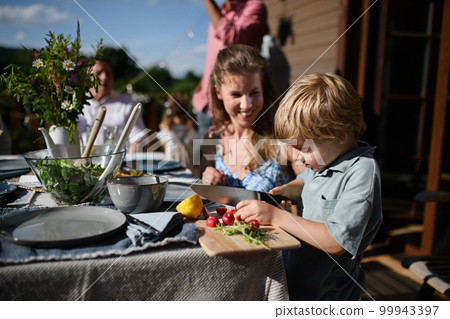 Happy family preparing for outdoor grill party, little boy cutting vegetable. Happy family preparing for outdoor grill party, little boy cutting vegetable. 99943397