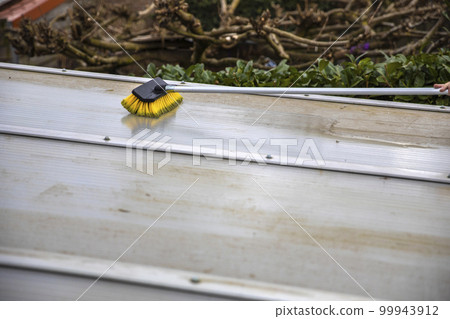 Washing the patio pergola roof cover made of aluminum. removing the dirty algae with brush soap and water close up in garden from a house terrace 99943912