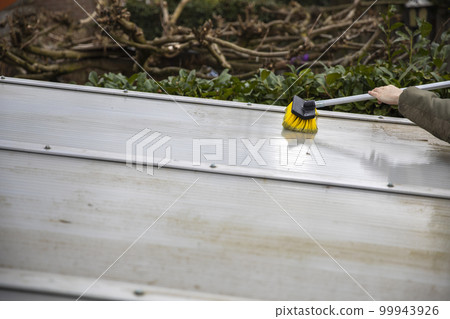 Washing the patio pergola roof cover made of aluminum. removing the dirty algae with brush soap and water close up in garden from a house terrace 99943926
