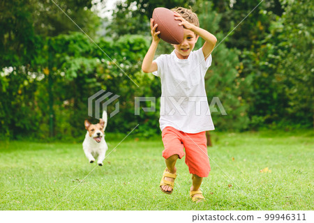 Kid playing american football ready to make touchdown and dog chasing him 99946311