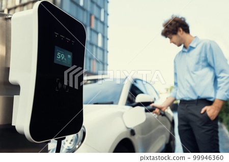 Progressive concept of focus EV car at charging station with blur man background Progressive concept of focus EV car at charging station with blur man background 99946360