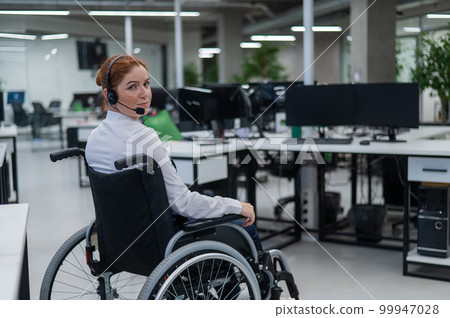 Caucasian woman moves around the office in a wheelchair. Female call center worker. Caucasian woman moves around the office in a wheelchair. Female call center worker. 99947028