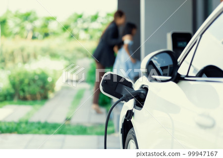Focus progressive EV car at home with blur woman in background. Focus progressive EV car at home with blur woman in background. 99947167
