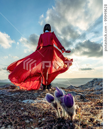 Rise of the mystic. sunset over the clouds with a girl in a long red dress. There is a dream grass in the meadow with purple flowers. 99949628