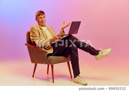 Portrait of mature, middle-aged man in jacket posing, working on laptop with emotive face over gradient pink purple background in neon light. Concept of emotions and lifestyle 99950332