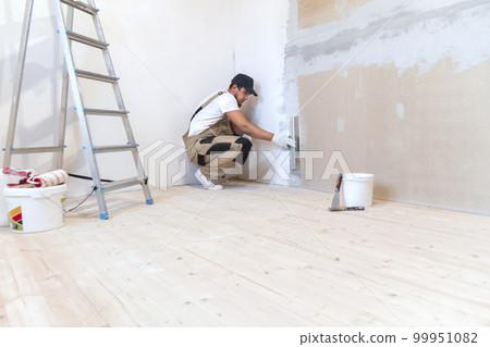 Male painter with a putty knife in his hands makes repairs in th 99951082