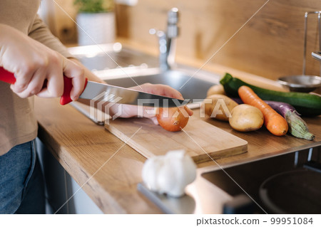 Side view of woman cutting an onion on a wooden board. Home food concept  99951084