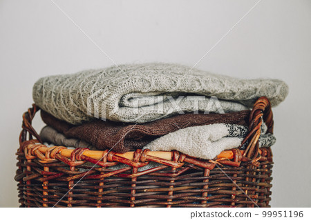 Stack of knitted sweaters on wicker basket. 99951196