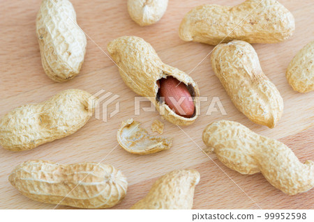 Variety of whole peanuts and one half peeled peanut with cracked shell on a wooden table Variety of whole peanuts and one half peeled peanut with cracked shell on a wooden table 99952598