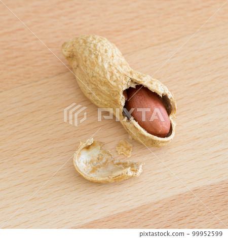 Half peeled peanut with cracked shell on a wooden table. 99952599