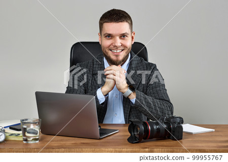 bearded male photographer smiling while working at her desk. bearded male photographer smiling while working at her desk. 99955767