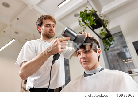 Professional hairdresser during work with man client with hair dryer in barber shop. Haircut in the barbershop. 99955963