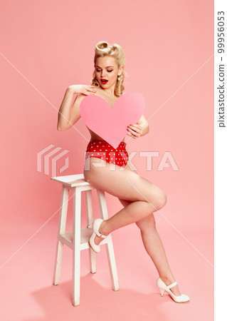 Summer vacation. Portrait of beautiful young girl in swimming suit posing against pink studio background. Concept of beauty and pin-up style Summer vacation. Portrait of beautiful young girl in swimming suit posing against pink studio background. Concept of beauty and pin-up style 99956053