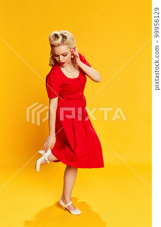 Portrait of beautiful young girl with stylish hairstyle in red suit posing against yellow studio background. Concept of beauty and pin-up style Portrait of beautiful young girl with stylish hairstyle in red suit posing against yellow studio background. Concept of beauty and pin-up style 99956129