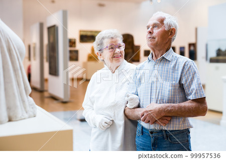 mature European couple examines paintings in an exhibition in hall of art museum 99957536