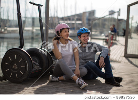 young couple guy and girl are walking on the segway along the board paved promenade in the port of a European city young couple guy and girl are walking on the segway along the board paved promenade in the port of a European city 99957550
