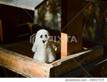 A small toy ghost stands in a bird feeder in the forest A small toy ghost stands in a bird feeder in the forest 99957575