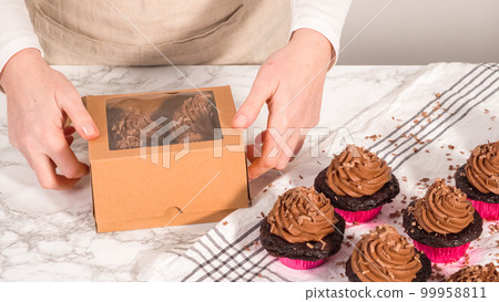 Step by step. Packaging chocolate cupcakes with chocolate ganache frosting into a paper cupcake box. 99958811