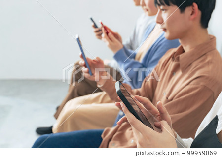 Young group looking at smartphones side by side Young group looking at smartphones side by side 99959069