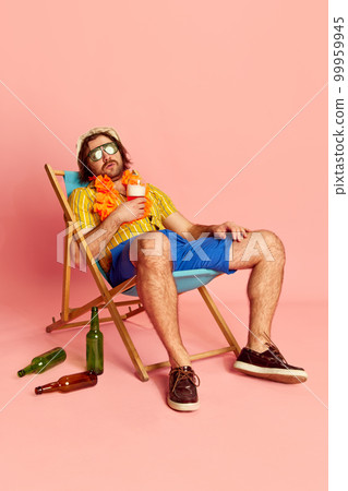 Tired beachgoer. Man in summer shirt and short with Hawaiian flower garland on chest sleeping on sun lounger over pink background. Vacation, summer, rest and male hobbies concept 99959945