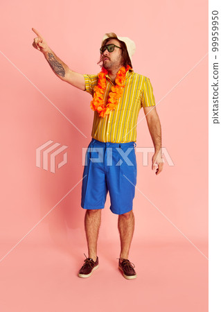 Exotic vacation. Man in summer shirt and short with Hawaiian flower garland on chest posing over pink background. Leisure activity, travel, summer, rest concept 99959950