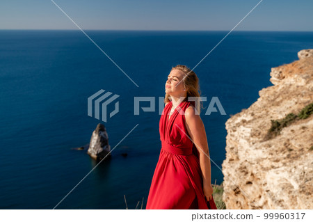 A woman in a red flying dress fluttering in the wind, against the backdrop of the sea. 99960317