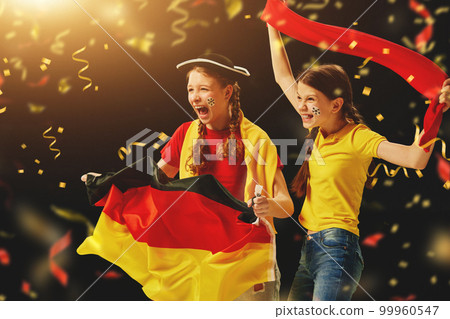 Excited young girls, teens emotionally cheering up favourite german football team on championship, game over dark background with confetti 99960547