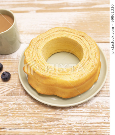 Baumkuchen, sakotis ,sekacz on wooden rustic table with cup of coffee, blueberries, traditional spit cake of lithuanian, polish, german, belarusian cuisine made of butter,eggs,flour,sugar. Vertical Baumkuchen, sakotis ,sekacz on wooden rustic table with cup of coffee, blueberries, traditional spit cake of lithuanian, polish, german, belarusian cuisine made of butter,eggs,flour,sugar. Vertical 99961330
