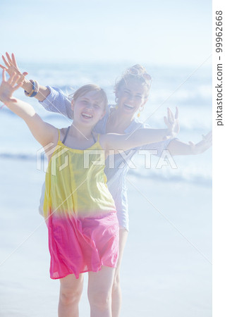 smiling mother and teenage daughter at beach having fun time 99962668