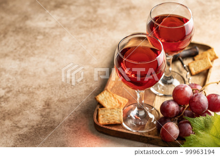 Two glasses of red wine, a bunch of red grapes, crackers and corkscrew on a wooden tray on beige textured background with text space. Party for two concept 99963194