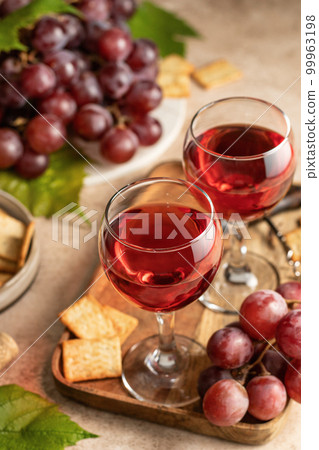 Two glasses of red wine, a bunch of red grapes, crackers and corkscrew on a wooden tray on beige textured background. Celebration party for two concept Two glasses of red wine, a bunch of red grapes, crackers and corkscrew on a wooden tray on beige textured background. Celebration party for two concept 99963198