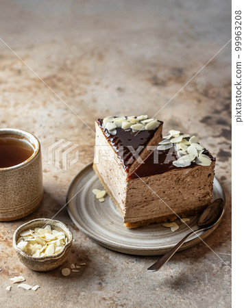 Two slices of chocolate cheesecake with almond petals, tea cup on brown textured background. Text space, menu 99963208