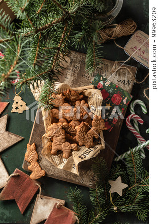 Christmas cookies or gingerbreads of patterned animal shapes on in wooden box on green wooden table. Xmas or new year rustic composition with fir tree and festive decor, top view 99963209