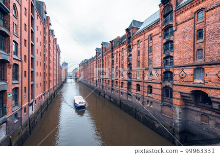 Touristic cruise boat on a channel with bridges in the warehouse district Speicherstadt in Hamburg, Germany 99963331