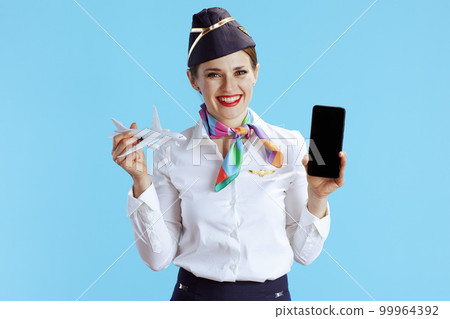 happy female stewardess on blue showing smartphone blank screen happy female stewardess on blue showing smartphone blank screen 99964392