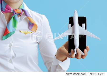 Female air hostess on blue showing airplane and smartphone 99964393