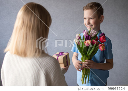 Cute boy gives a bouquet of tulips and a box with a gift to mom Cute boy gives a bouquet of tulips and a box with a gift to mom 99965224