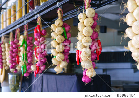 Garlic, onion and chilli, autumn season product, hanging on wooden logs in kitchen 99965494