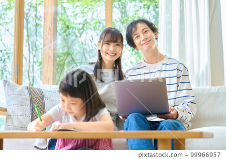 一對年輕夫婦在客廳裡看著孩子學習，同時看著電腦 99966957