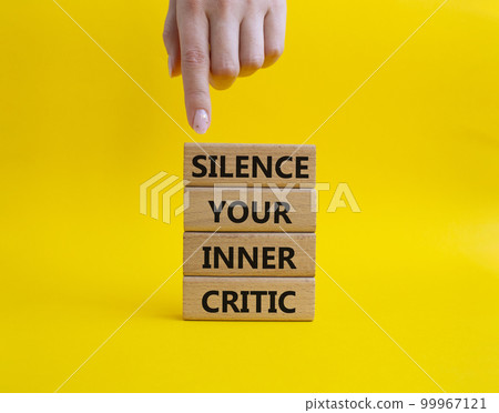 Silence your inner critic symbol. Wooden blocks with words Silence your inner critic. Beautiful yellow background. Businessman hand. Business and Silence your inner critic concept. Copy space. 99967121
