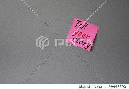 Tell your story symbol. Concept words Tell your story on pink steaky note. Beautiful grey background. Business and Tell your story concept. Copy space. 99967200