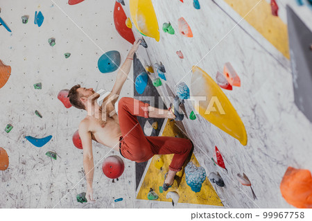 Young climber climbing on the boulder wall indoor, rear view, concept of extreme sports and bouldering Young climber climbing on the boulder wall indoor, rear view, concept of extreme sports and bouldering 99967758