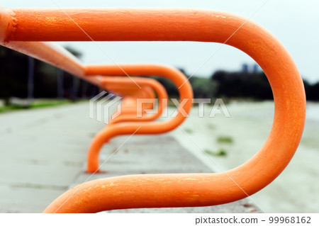Abstract background. Blurred curved railing of the promenade going into the distance. The metal is painted orange. Abstract background. Blurred curved railing of the promenade going into the distance. The metal is painted orange. 99968162
