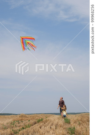 The father and the girls are flying a kite in a mown wheat field. Kids have fun spending the weekend with Dad. The father and the girls are flying a kite in a mown wheat field. Kids have fun spending the weekend with Dad. 99968256