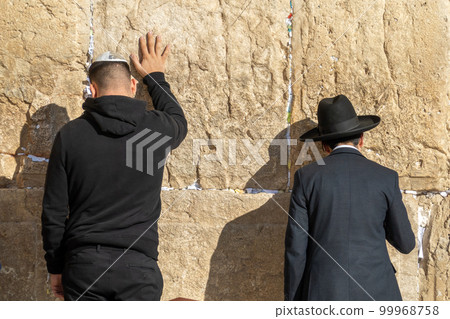Man in kippah praying with hand on holy wall Man in kippah praying with hand on holy wall 99968758