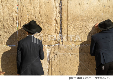 Men facing holy stone wall while praying 99968759